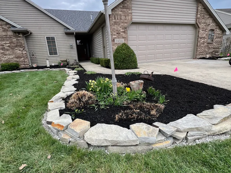 Lamp post set in a boulder ringed mulch bed in front of a garage