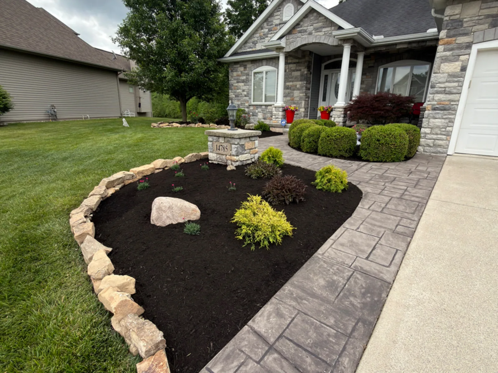 Boulder edged landscape bed alongside a stamped concrete walkway at a suburban home